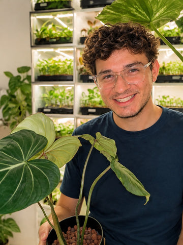 Nick, Mitgründer von Mini Houseplants, mit einem Philodendron vor den Anzuchtschränken